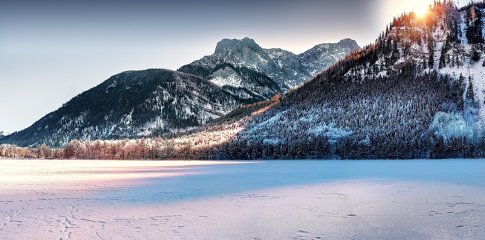Snowy mountains with sunlit forest and frozen lake