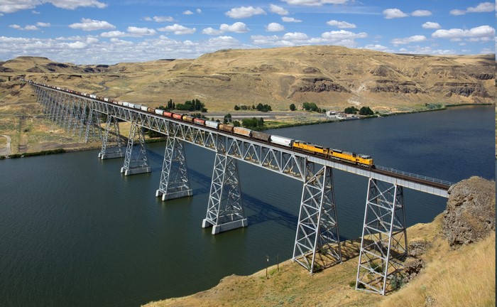Train crossing a long bridge over a river in a dry landscape