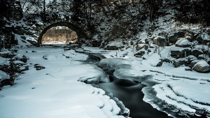 Winter stream under stone bridge with ice and snow