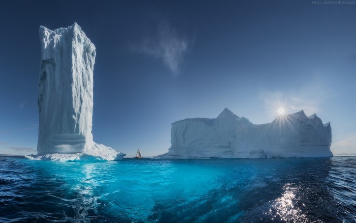 Icebergs and sailboat in Greenland under sun rays