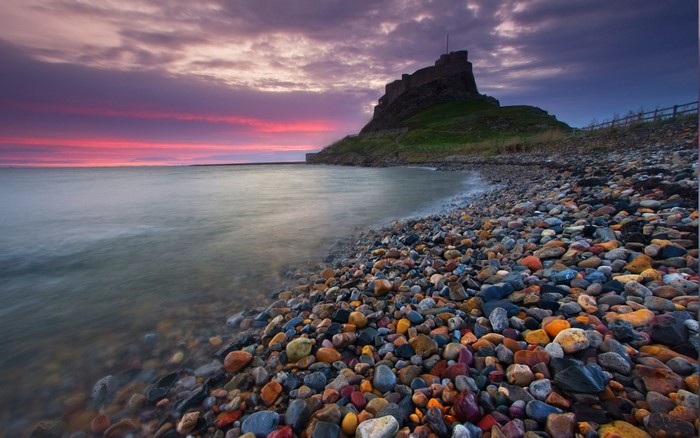 Lindisfarne Castle on a rocky beach at sunset