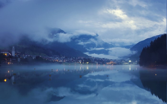 Misty lake reflecting mountains and a town at dusk