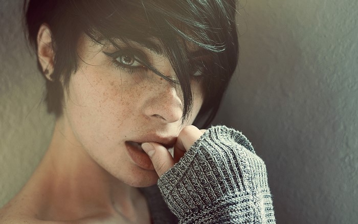 Woman with dark hair and freckles biting her finger