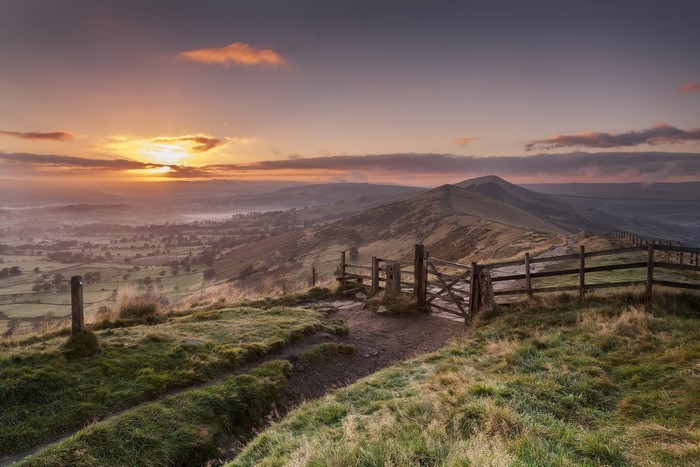 Sunrise over a misty valley with a wooden gate and fence