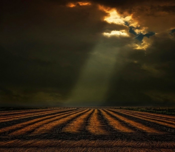 Sun rays piercing through dark clouds over a harvested field