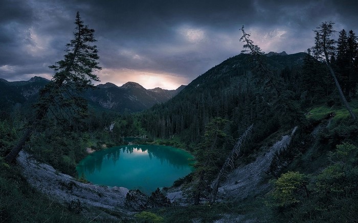 Turquoise lake in a mountain forest under stormy sunset sky