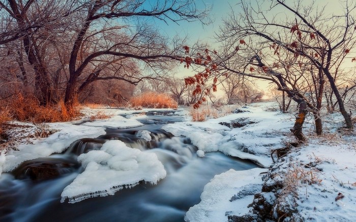 Winter river flowing through snow-covered trees at sunset