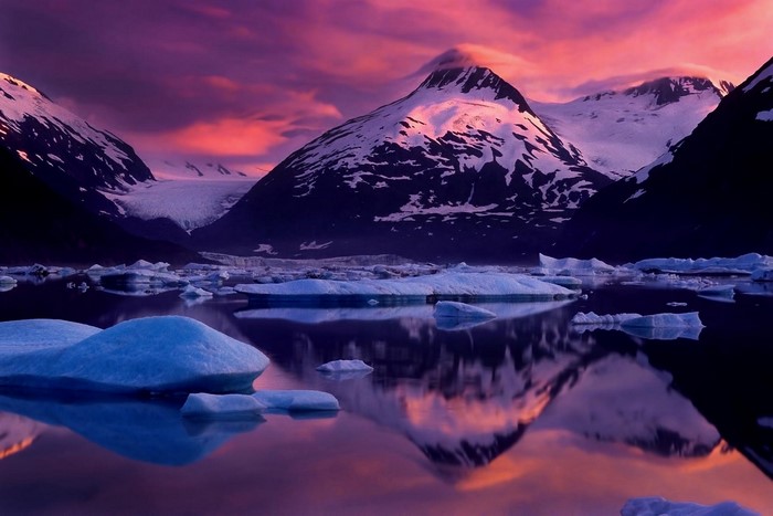 Snowy mountains and icebergs reflecting in water at sunset