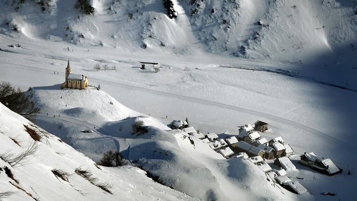 Snowy mountain village with church and skiers