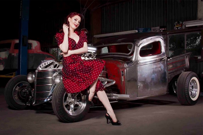 Woman in polka dot dress posing with a hot rod car