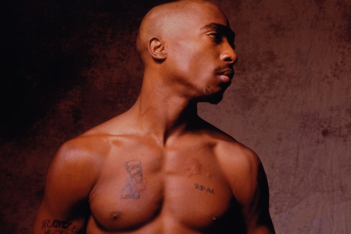 2Pac Shirtless with Tattoos Against Dark Background