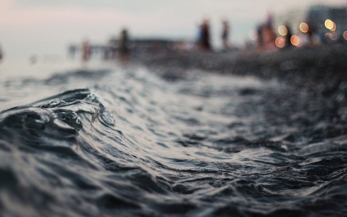 Close-up of a wave with blurred beachgoers in the background