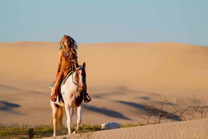 Woman in Native American Headdress Riding Horse in Desert