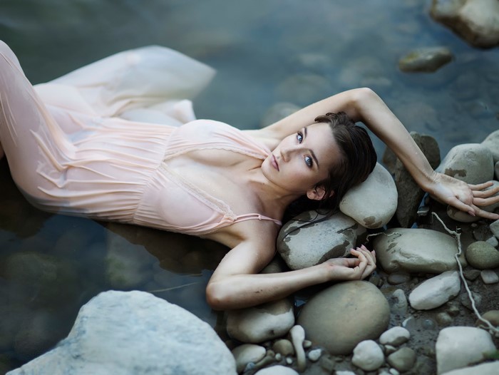 Woman in wet dress lying in water with rocks
