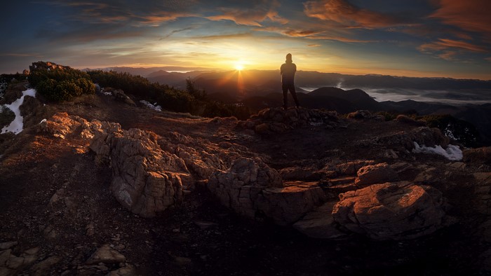 Man on mountain peak watching sunset over misty landscape