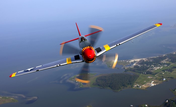 North American P-51 Mustang flying over a coastline
