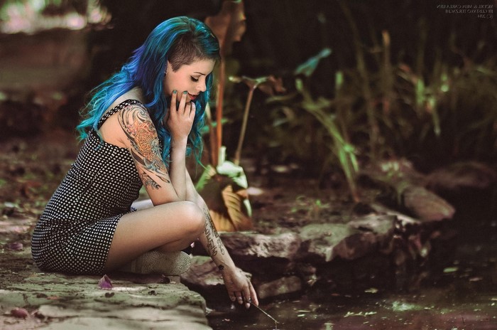 Woman with blue dyed hair and tattoos sitting by water
