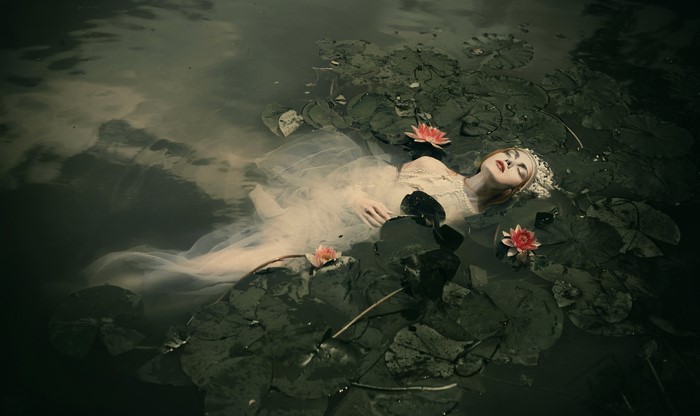 Woman in white dress floating among water lilies