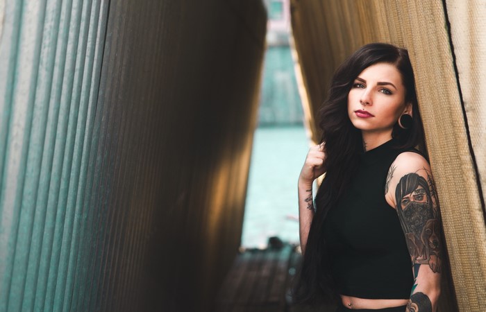 Woman with tattoos leaning against a wall