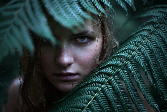 Woman peeking through wet fern leaves