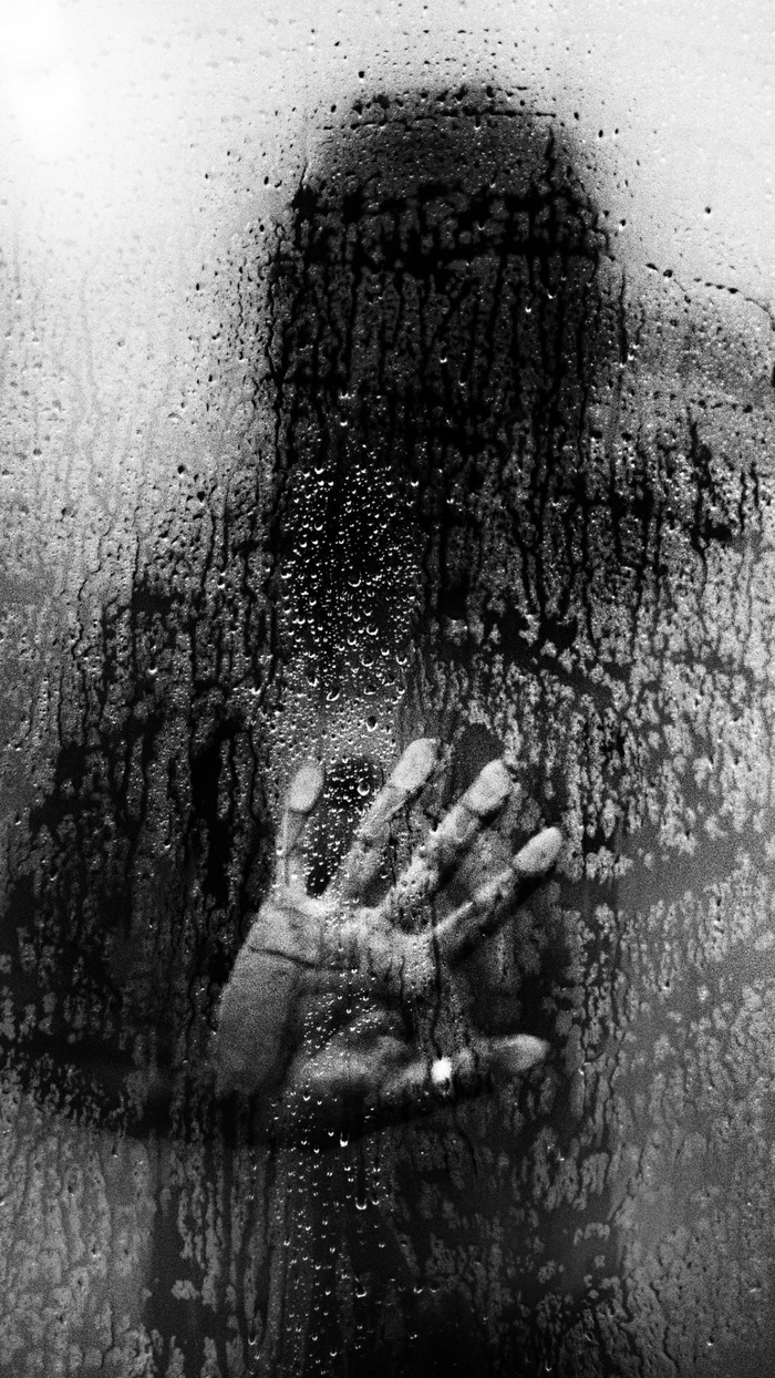 Silhouette of a person with handprint on wet glass
