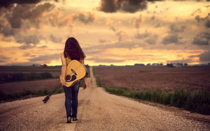 Woman with curly hair carrying a guitar on a road