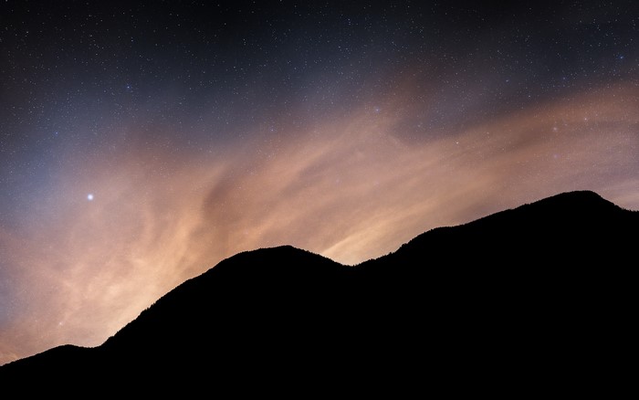 Night sky with stars and clouds over mountains