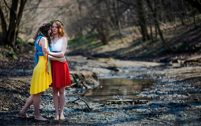 Two women embracing in a forest by a stream