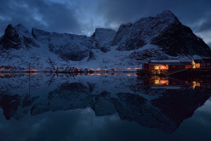 Winter village with snow-capped mountains reflected in a calm lake