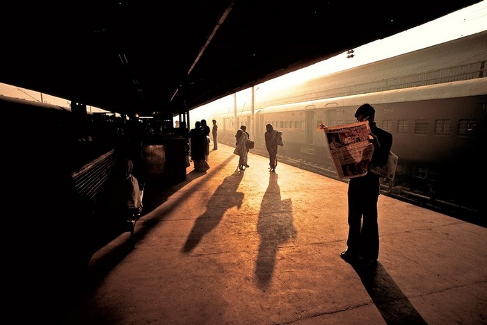 People at a train station reading newspapers at sunset