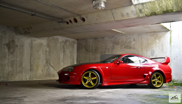 Red Toyota Supra with gold rims in parking garage