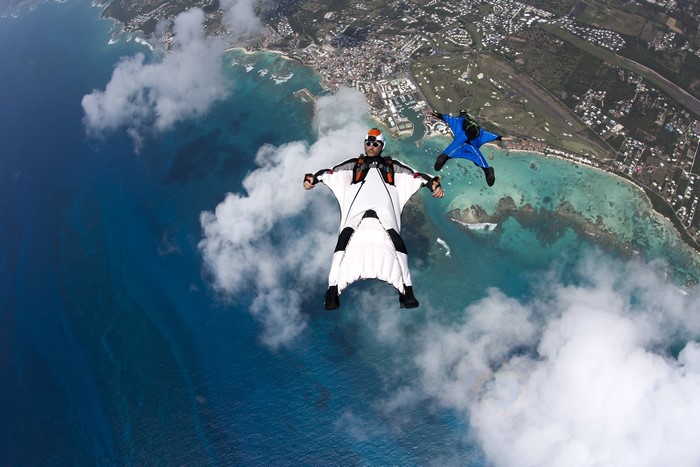 Two people wingsuit flying over a tropical coastline