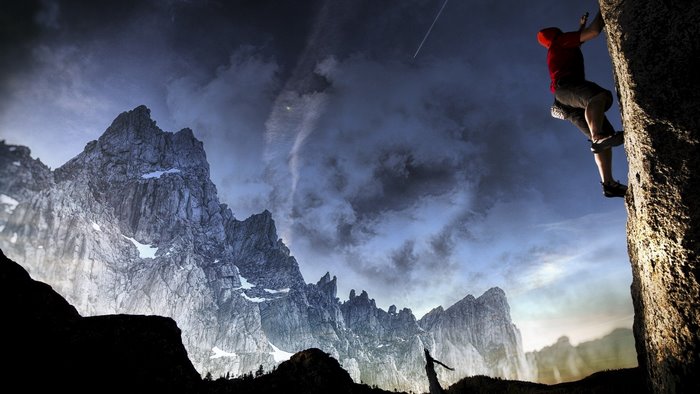 Man rock climbing a mountain with dramatic clouds