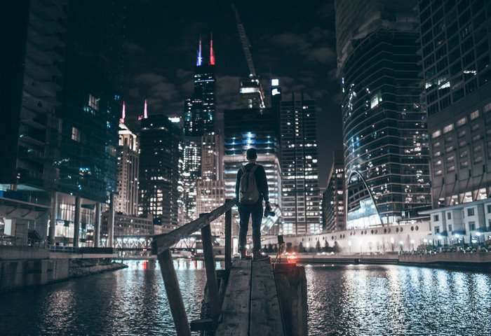 Man with backpack and camera on wooden pier overlooking Chicago cityscape at night