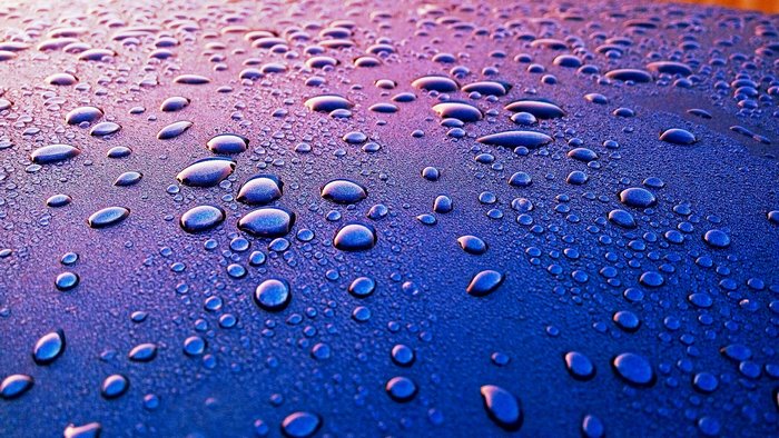 Water drops on a blue surface with purple lighting