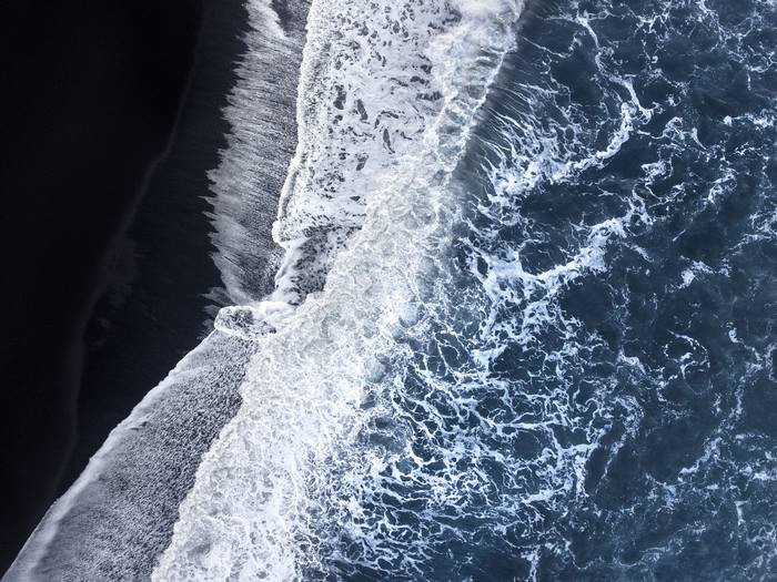 Aerial view of waves crashing on a black sand beach
