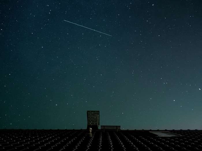 Starry night sky over a house roof with a chimney