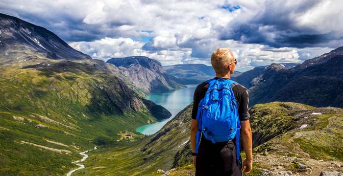 Man with blue backpack overlooking Norwegian fjord and mountains