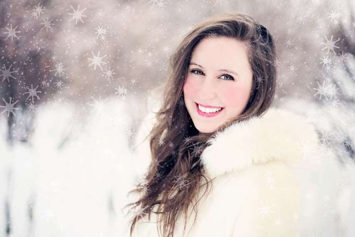 Pretty woman in white fur coat smiling in snow