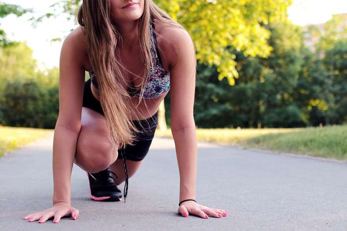 Woman in sports bra and shorts in starting position outdoors