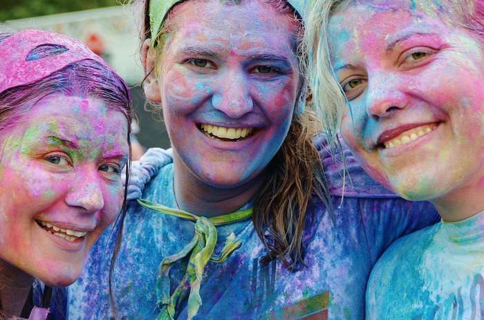 Three smiling women covered in colorful powder