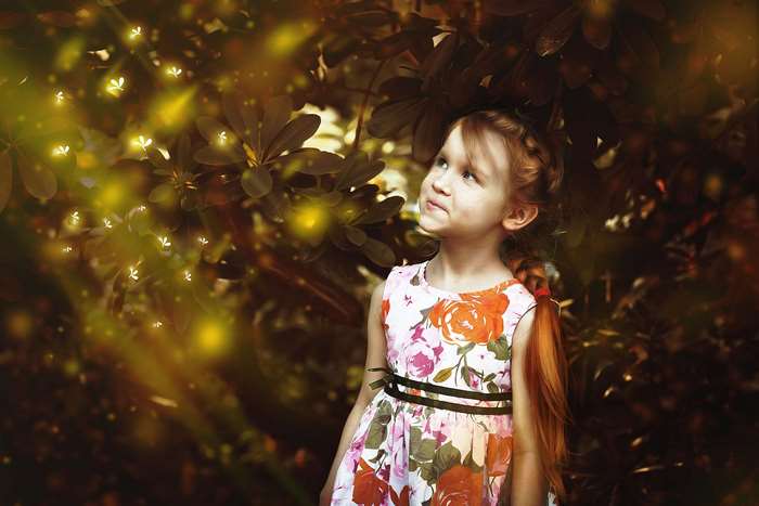 Girl in a floral dress looking at fireflies in a forest