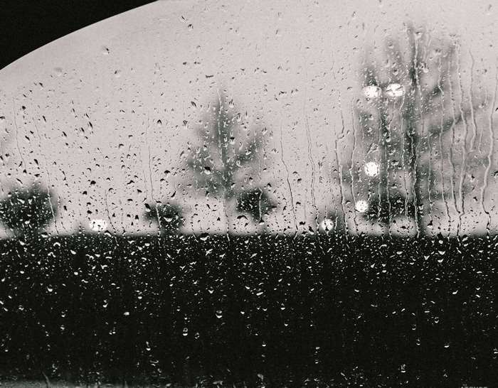 Raindrops on a window with blurred trees and lights