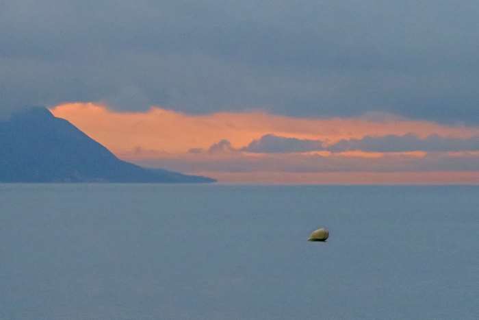 Sunset over the water with a mountain and a buoy