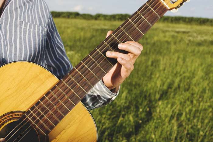 Person playing acoustic guitar in a grassy field