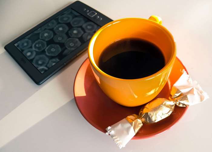 Kindle, coffee cup, and candy on a saucer