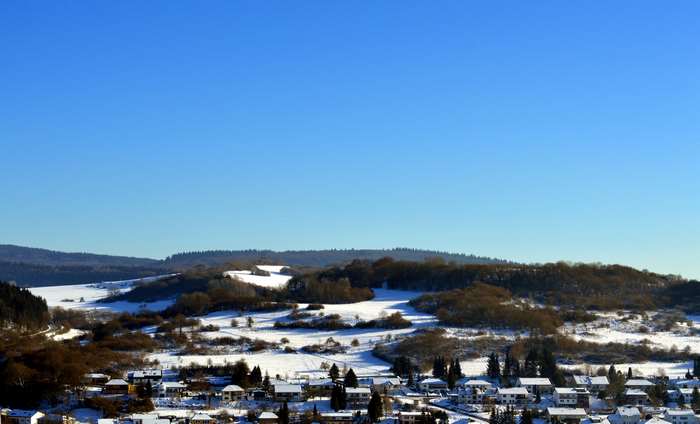 Winter landscape with snow-covered hills and houses in Eifel, Germany