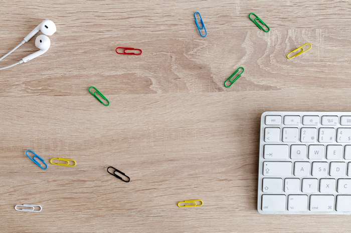 Earbuds and keyboard on a wooden desk with paperclips