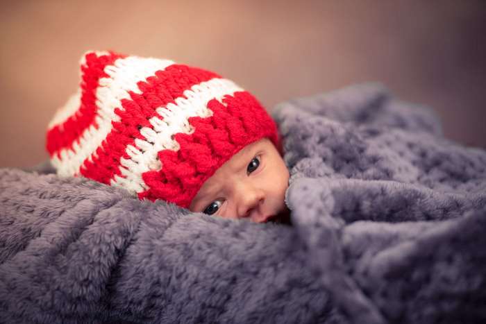 Newborn baby wearing a red and white striped hat wrapped in a blanket