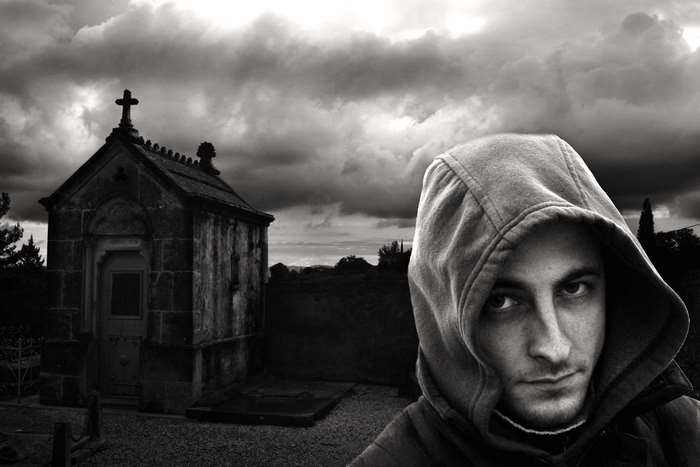 Man in hoodie in front of a chapel in a cemetery
